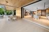 Seamless indoor-outdoor connection via pocket sliding glass doors opening from chef's kitchen and dining area to covered wood-ceiling loggia with outd