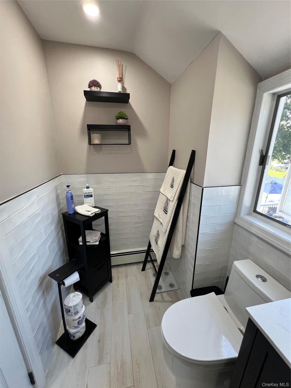 Light wood-finish flooring, white subway tile wainscoting, and a window for natural light