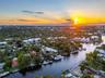 Sweeping aerial sunset view of deep-water canal with property and private dock visible, large motor yacht docked, lush tropical neighborhood, and vibr