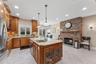 Kitchen featuring glass insert cabinets, brown cabinetry, pendant lighting, light stone countertops, and recessed lighting