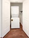 Laundry area with dark wood finished floors and stacked washing machine and dryer