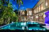 Nighttime pool view featuring illuminated lap pool with dark mosaic tile, elevated spa with spillover, teak chaise lounges, cantilever umbrella, floor