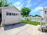 Detached garage with upper window panels, concrete driveway, and a fenced grassy yard. ai generated