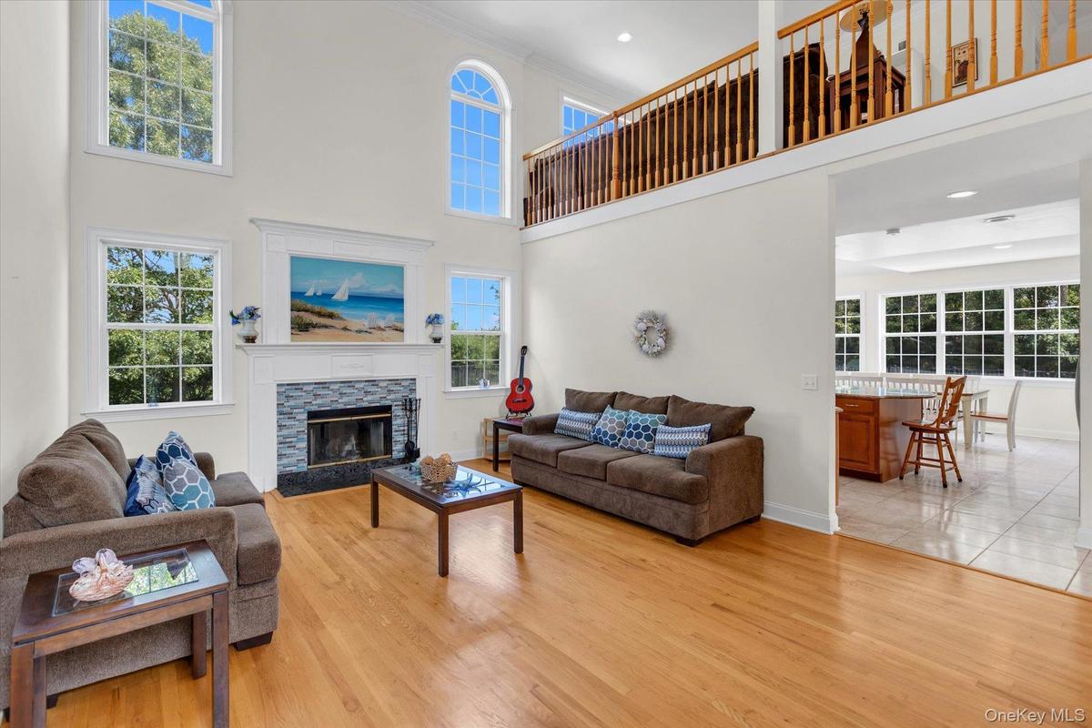 Two-story living area with hardwood flooring, a fireplace featuring a stone surround and hearth, and an upper-level railing overlooking the living roo