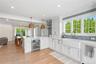 Kitchen featuring a peninsula, decorative light fixtures, white cabinetry, beverage cooler, and light stone counters