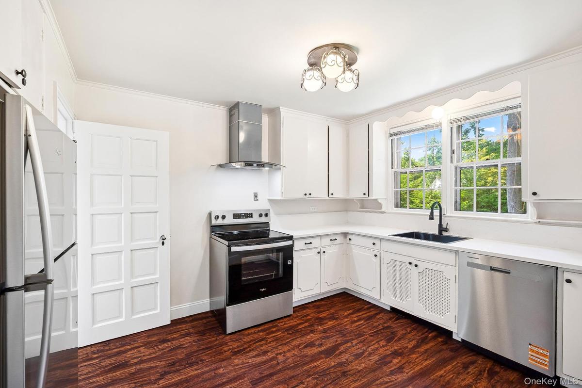 Kitchen featuring appliances with stainless steel finishes, wall chimney range hood, dark wood-style flooring, ornamental molding, and light counterto