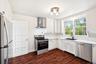 Kitchen featuring appliances with stainless steel finishes, wall chimney range hood, dark wood-style flooring, ornamental molding, and light counterto