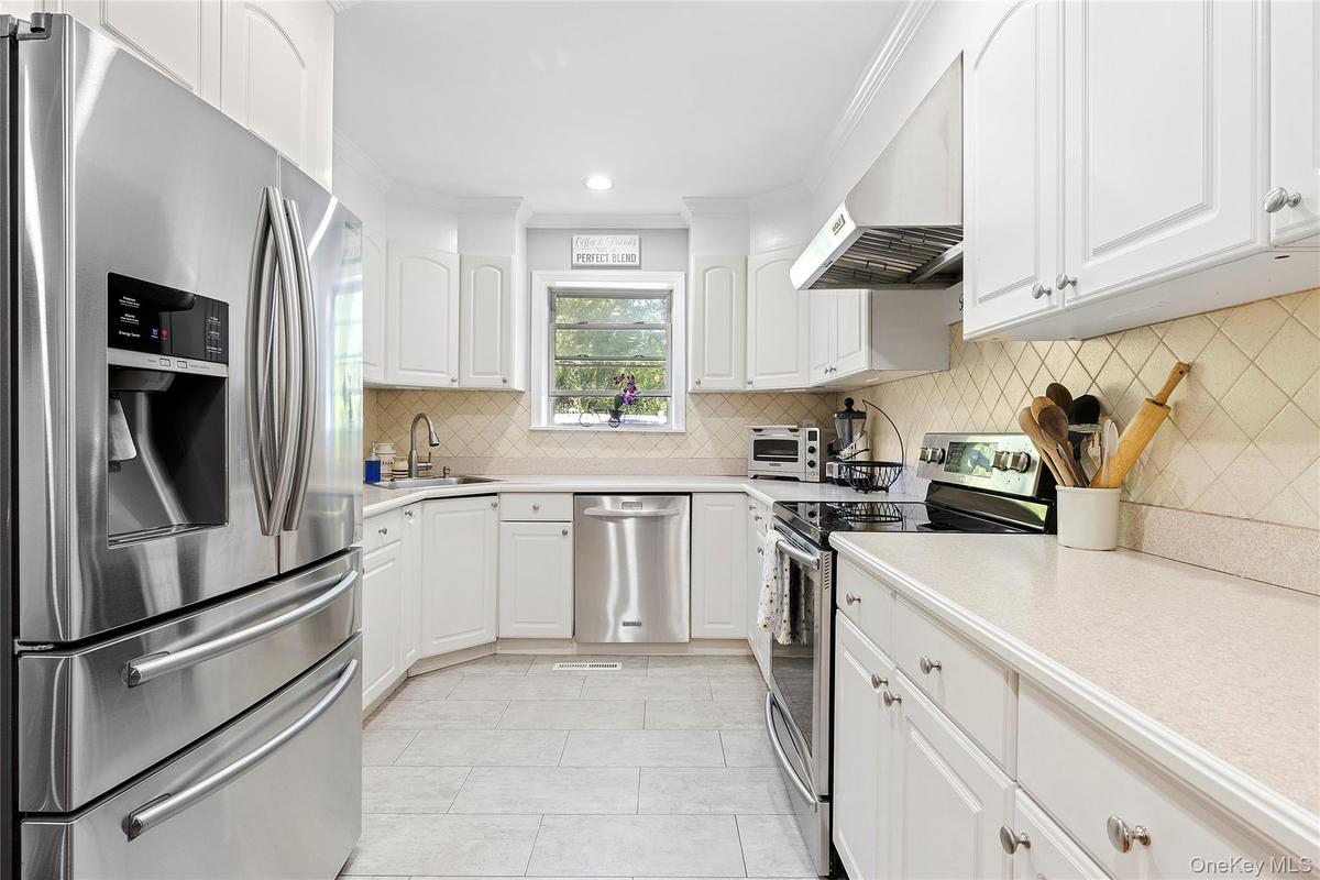 Kitchen featuring appliances with stainless steel finishes, white cabinets, light countertops, range hood, and recessed lighting