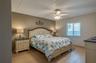 This spacious bedroom offers warm neutral tones, a ceiling fan for added comfort, and a large window that brings in natural light. The room’s layout a