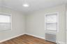 Bright interior space featuring two windows with horizontal blinds, wood-finish flooring, and a flush-mount ceiling light