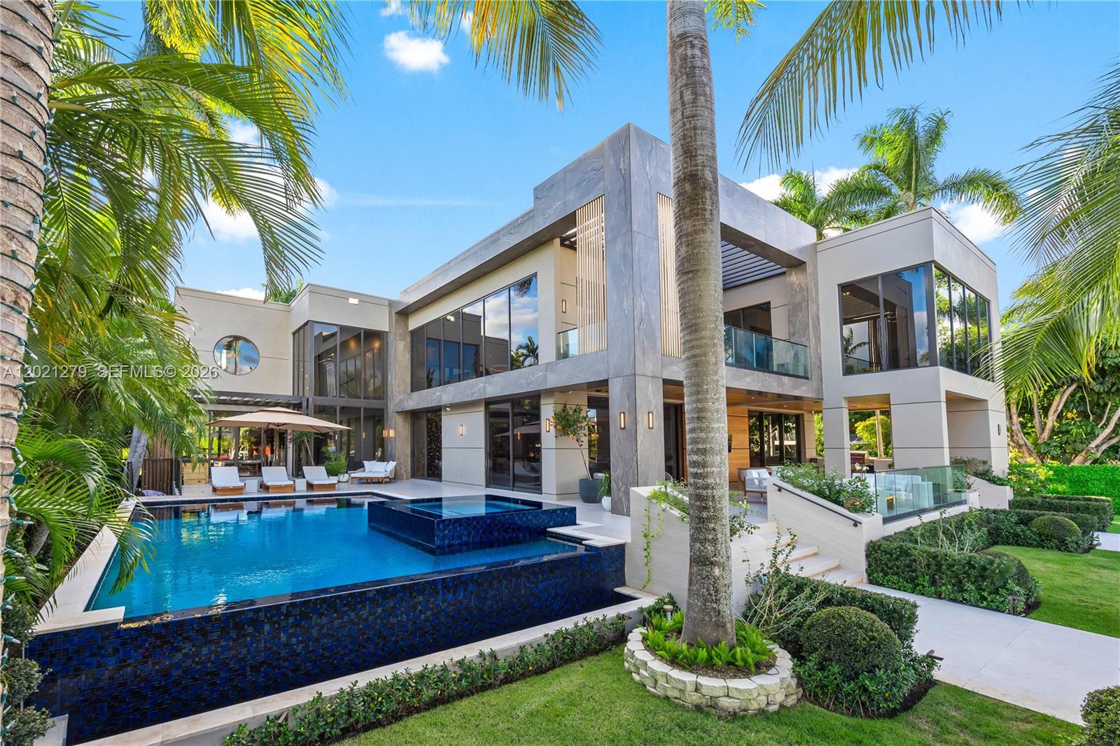 Resort-style pool and spa with dark mosaic tile, sun deck with chaise lounges, pergola, manicured lawn, tropical landscaping, and full two-story moder