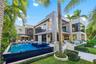 Resort-style pool and spa with dark mosaic tile, sun deck with chaise lounges, pergola, manicured lawn, tropical landscaping, and full two-story moder