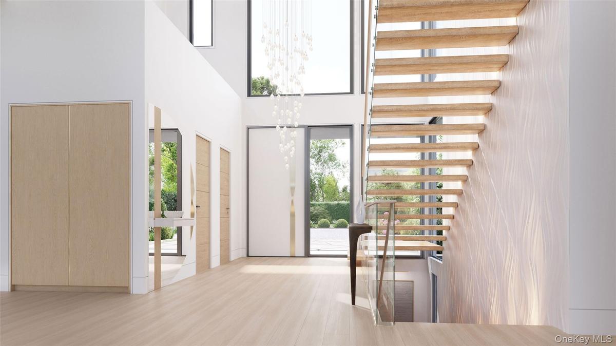 A striking custom pivot door opens to a light-filled foyer defined by floating stairs and seamless white oak flooring. With a discreet powder room and