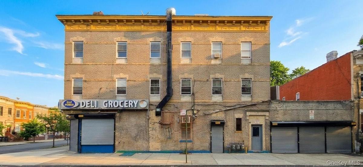 Brick facade building featuring ground-floor retail space with a roll-down security gate, multiple windows on upper levels, and an ornate cornice