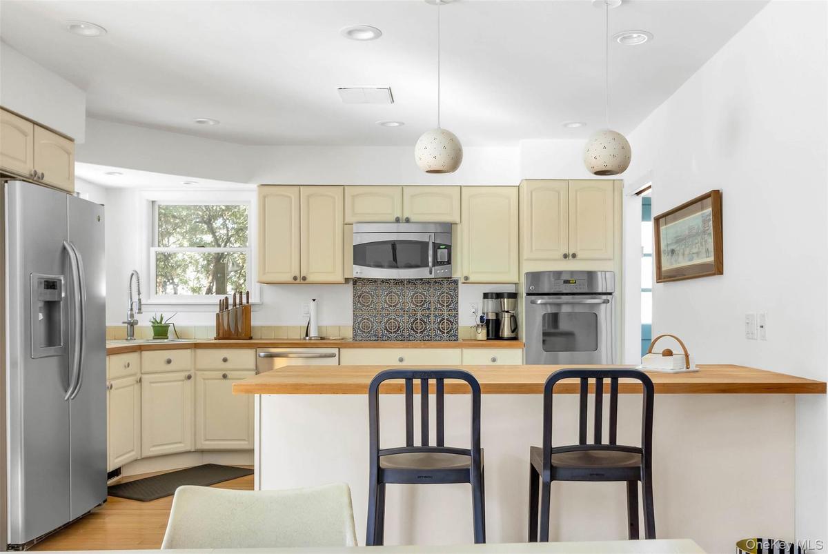 Kitchen with wood counters, decorative light fixtures, sink, stainless steel appliances, and cream cabinets