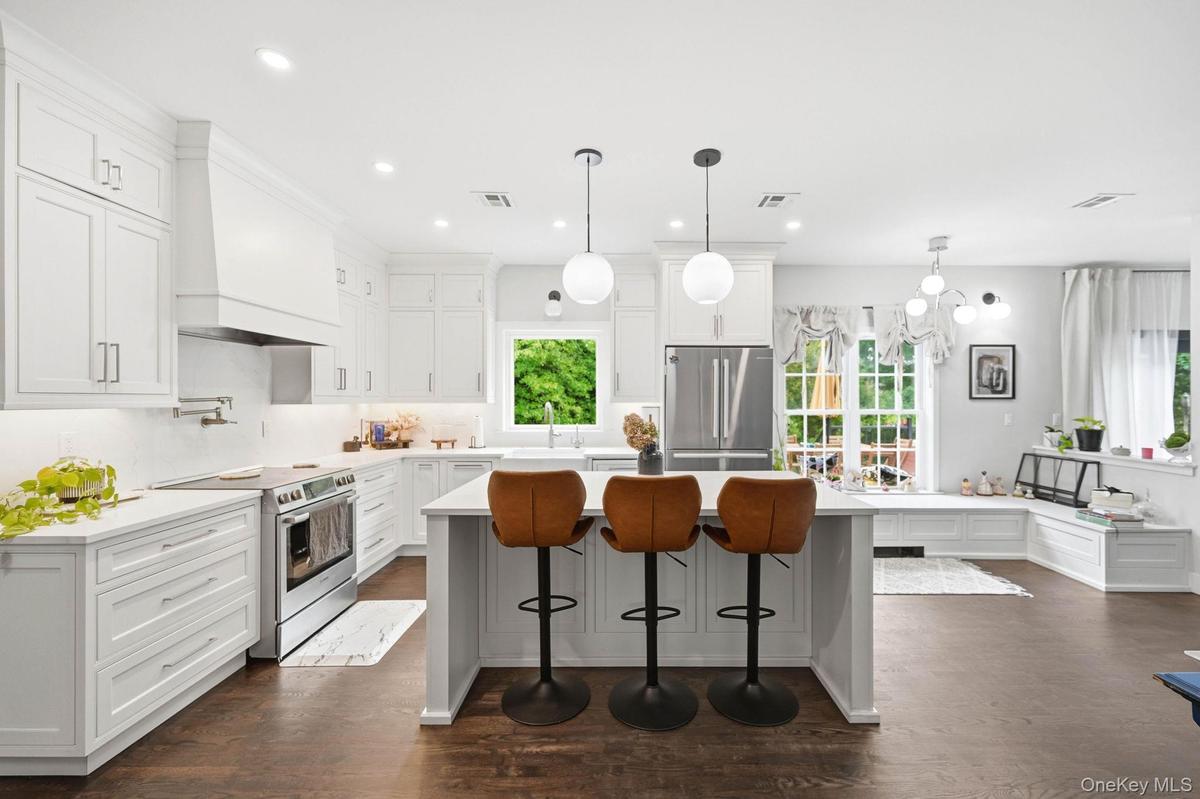 A bright, beautifully updated open-concept kitchen featuring custom white cabinetry, sleek countertops, stainless-steel appliances and a spacious cent
