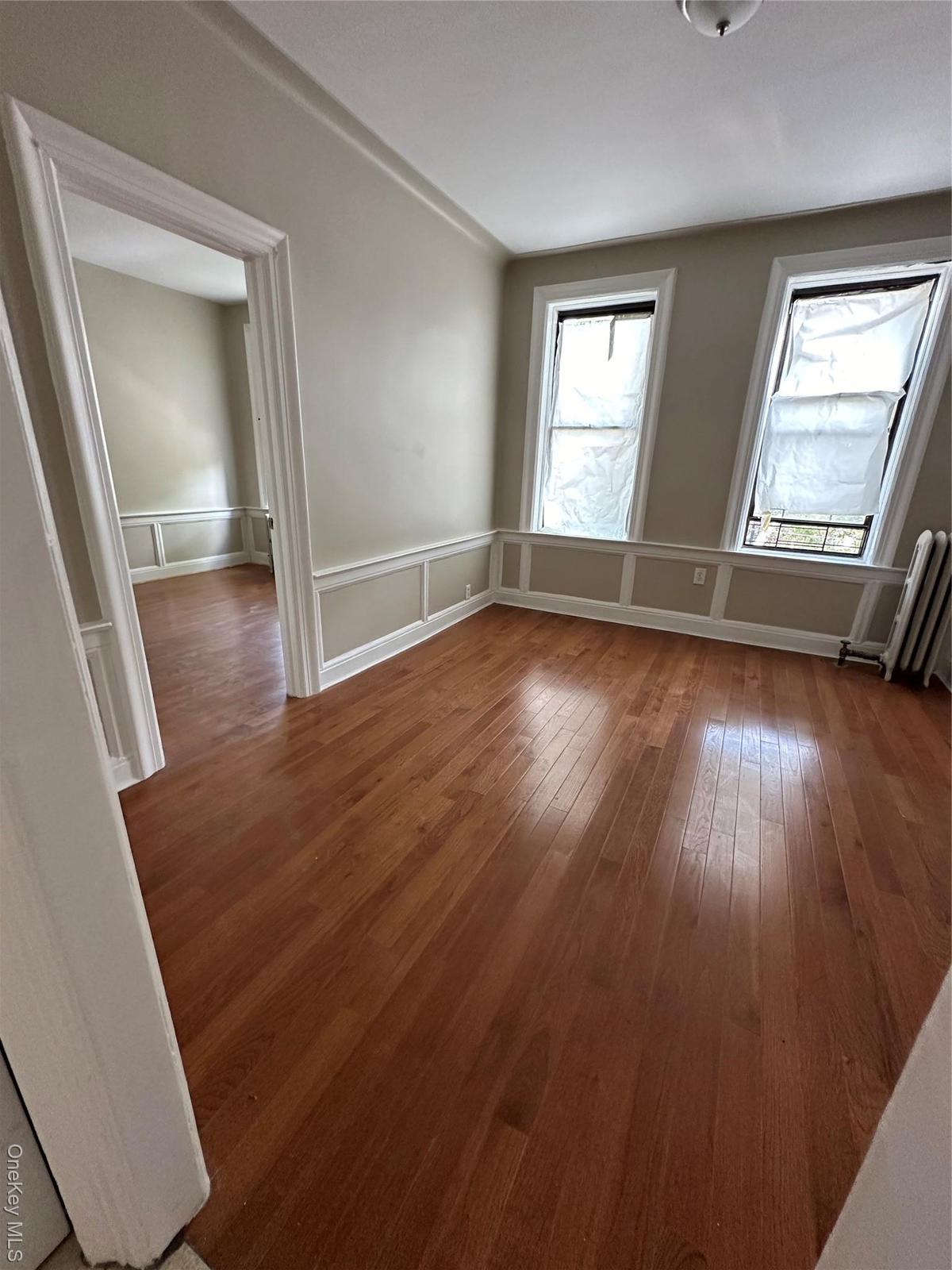 Empty room with light wood-type flooring, radiator, a decorative wall, healthy amount of natural light, and a wainscoted wall