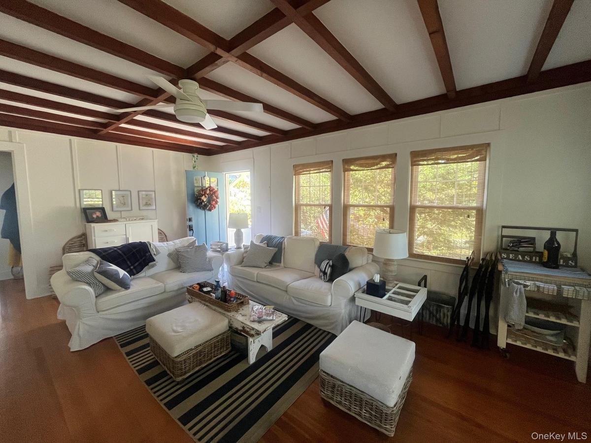 Living area featuring beamed ceiling, dark wood-type flooring, plenty of natural light, ceiling fan, and a decorative wall