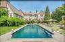 This grand Tudor estate features a resort-caliber outdoor oasis centered around a sophisticated dark-bottom pool and a striking geometric stone terrac