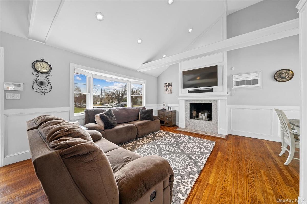 Living room with a wainscoted wall, a decorative wall, wood finished floors, lofted ceiling, and a fireplace with flush hearth