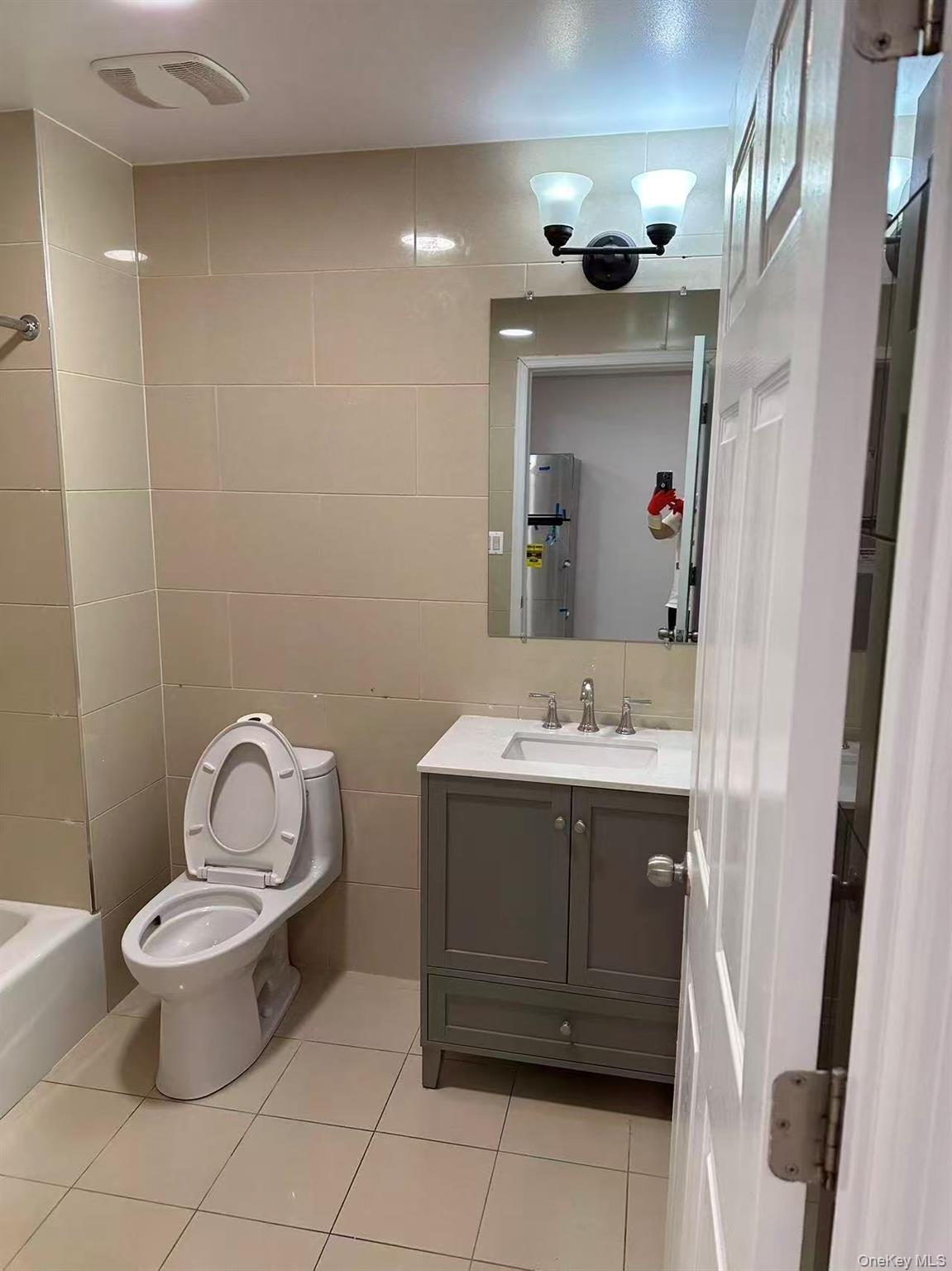 Bathroom with tile walls, light tile patterned floors, vanity, and bathtub / shower combination