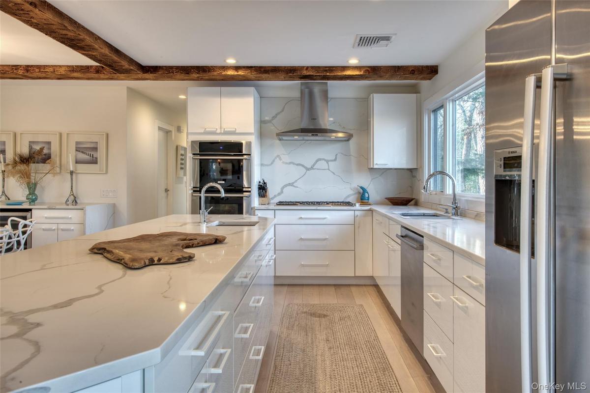 Kitchen featuring wall chimney exhaust hood, a sink, beam ceiling, stainless steel appliances, and backsplash