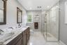 Bathroom featuring a marble finish shower, light marble finish flooring, double vanity, and recessed lighting