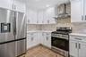 Modern kitchen featuring white shaker cabinetry with black hardware, stainless steel appliances, light-toned stone backsplash, and light-toned counter