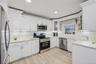 Kitchen featuring appliances with stainless steel finishes, white cabinets, glass insert cabinets, decorative backsplash, and light stone countertops