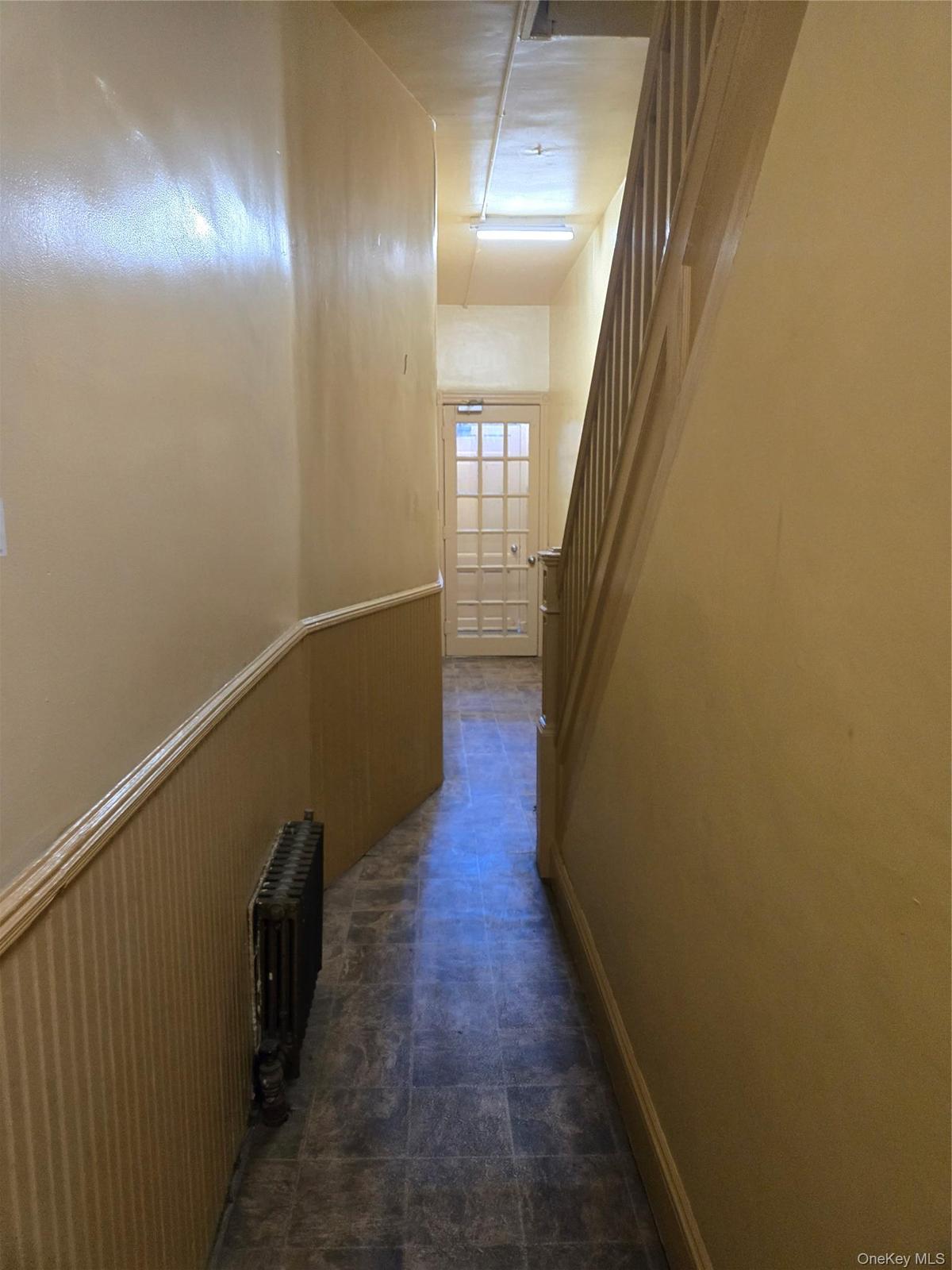 Hallway featuring stairway, radiator, and a wainscoted wall