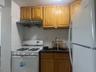 Kitchen featuring white appliances, brown cabinets, tasteful backsplash, range hood, and dark stone counters