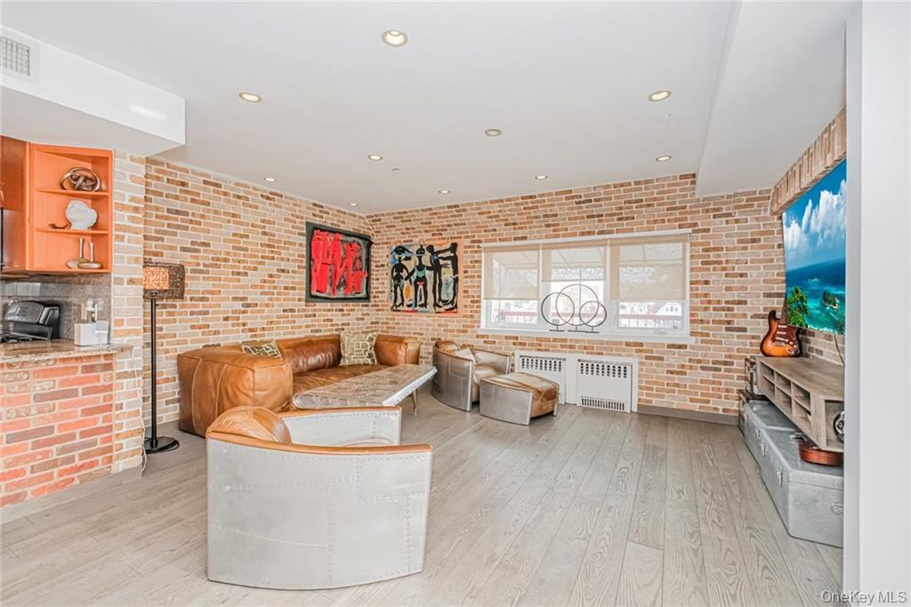 Living room with light wood finished floors, recessed lighting, radiator, and brick wall