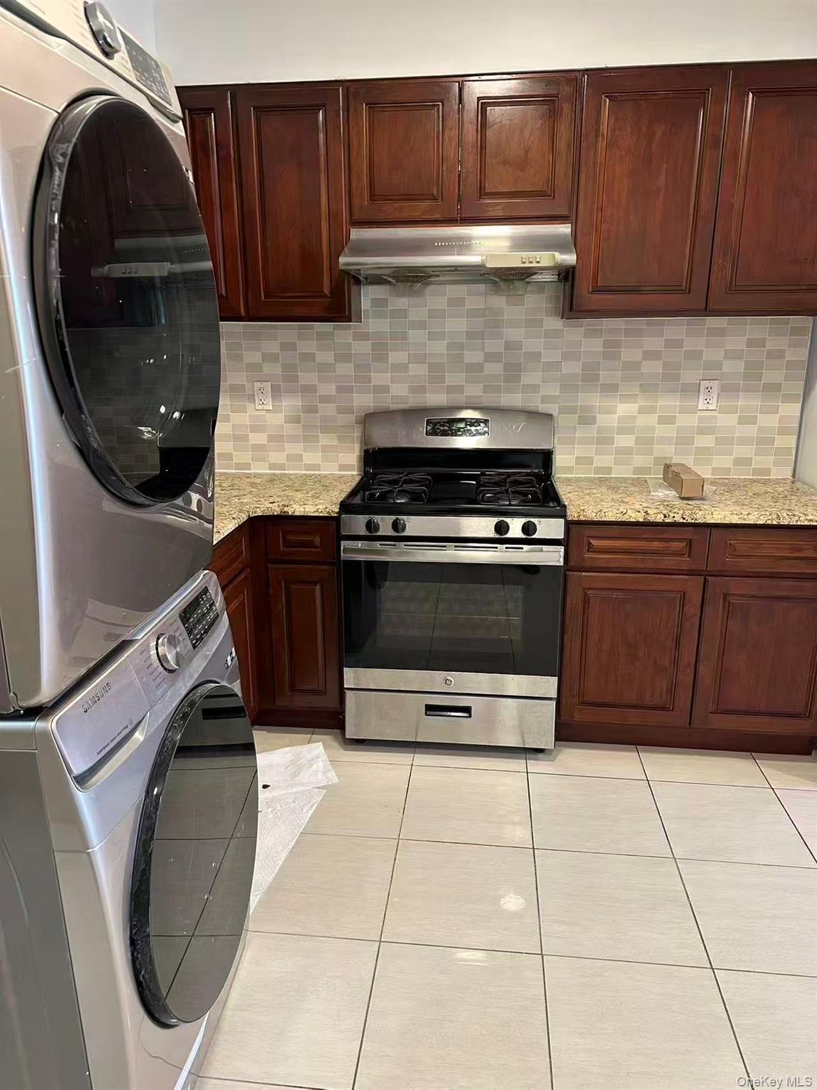Kitchen featuring stainless steel range with gas stovetop, light tile patterned floors, decorative backsplash, under cabinet range hood, and dark brow