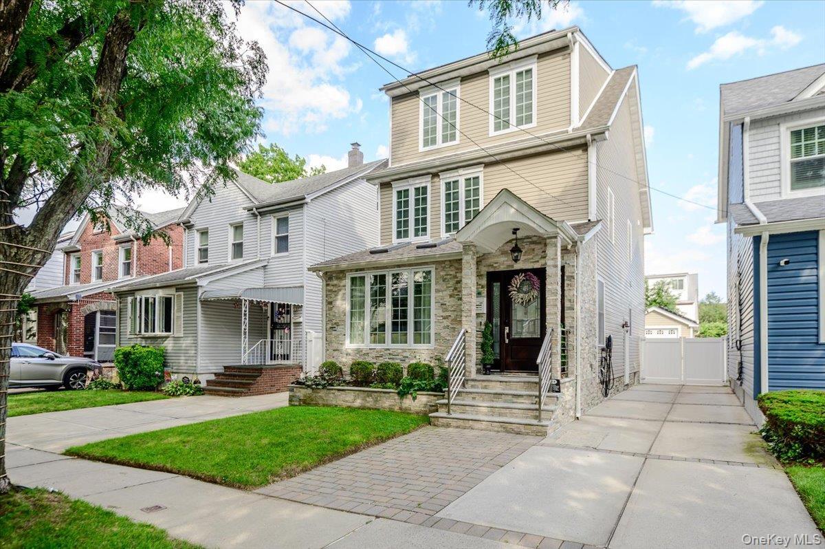 Stone facade with an inviting covered entryway, prominent front windows, and a paved driveway leading to a private rear gate