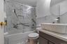 Bathroom featuring a shower-tub combination with sliding glass doors, a built-in shower niche, and a wall of marble-patterned tile