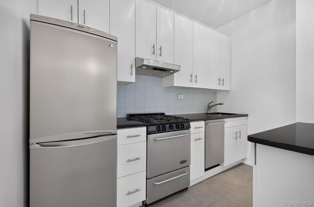 Streamlined kitchen featuring white cabinetry, dark countertops, stainless steel appliances, a tile backsplash, and wood-finish flooring