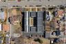 Aerial view showcasing a multi-building property with extensive flat roofing, multiple asphalt parking areas, and mature trees on the perimeter