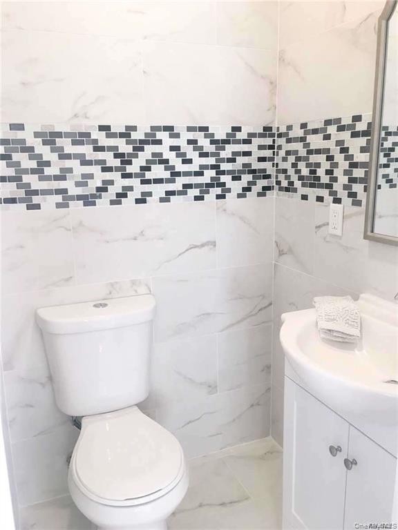 Spa-inspired bathroom featuring marble-look wall tile, a discrete mosaic tile accent band in charcoal and white tones, a white porcelain toilet with e