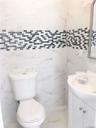 Spa-inspired bathroom featuring marble-look wall tile, a discrete mosaic tile accent band in charcoal and white tones, a white porcelain toilet with e
