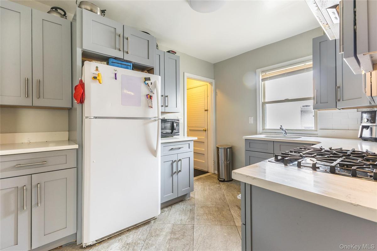 Kitchen with gray cabinetry, freestanding refrigerator, light countertops, and stovetop