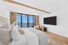 Primary bedroom with wood-beam ceiling accent, floor-to-ceiling windows, motorized blinds, and a private screened balcony framing open Tampa Bay views