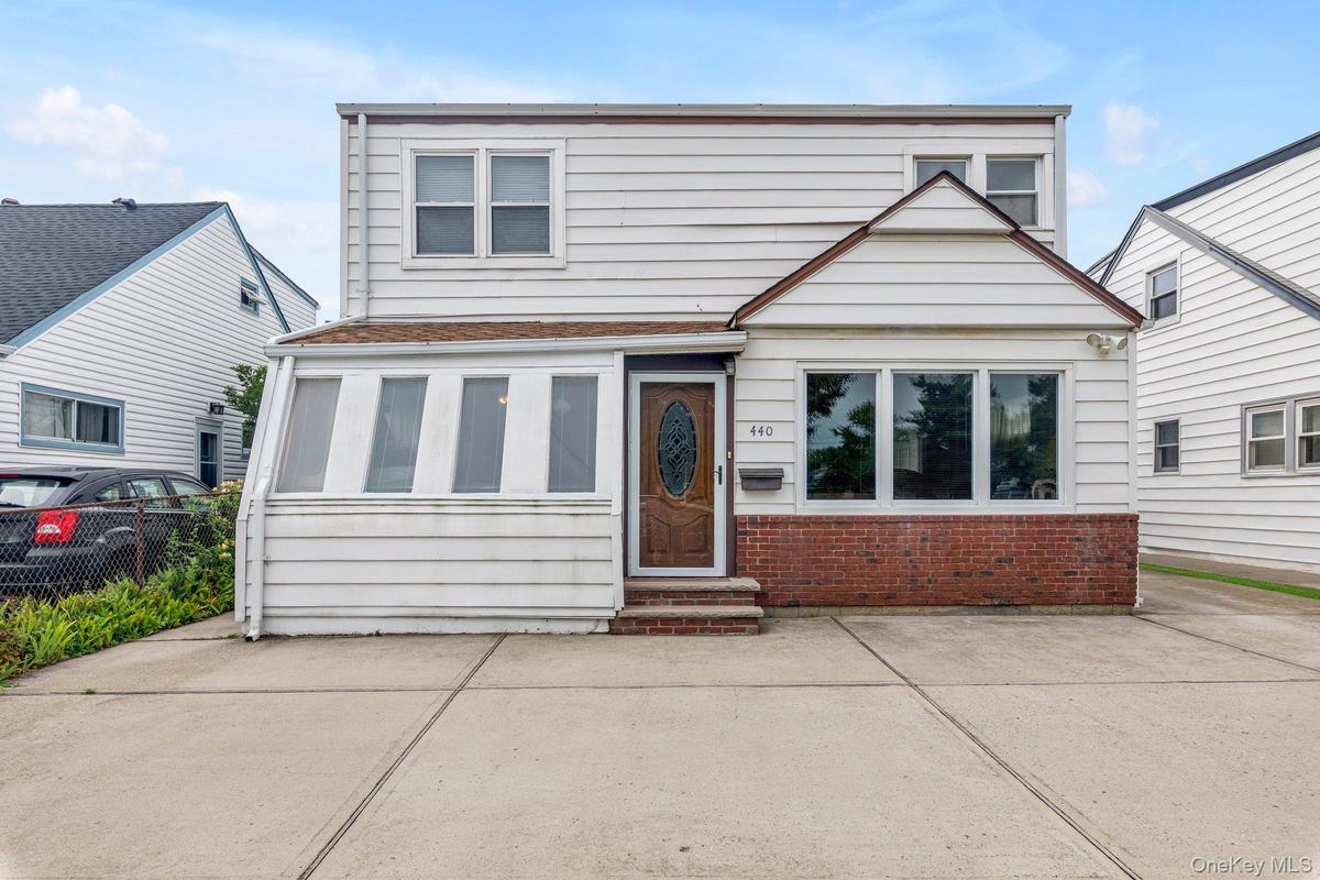 Exterior with white siding, red brick accents, a wood-finish front door, and multiple windows, large driveway