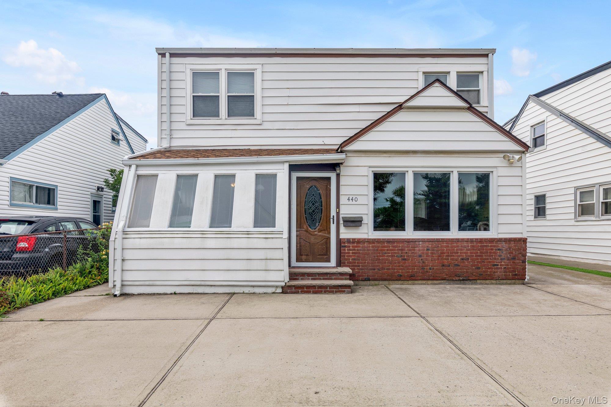 Exterior with white siding, red brick accents, a wood-finish front door, and multiple windows, large driveway
