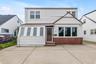 Exterior with white siding, red brick accents, a wood-finish front door, and multiple windows, large driveway