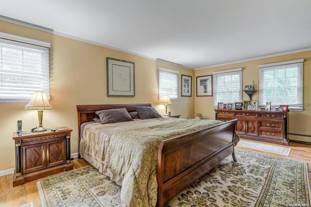 Bedroom with ornamental molding, light wood-type flooring, and baseboard heating