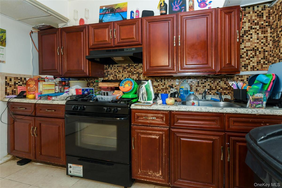 Kitchen with dark brown cabinets, backsplash, black gas stove, and under cabinet range hood