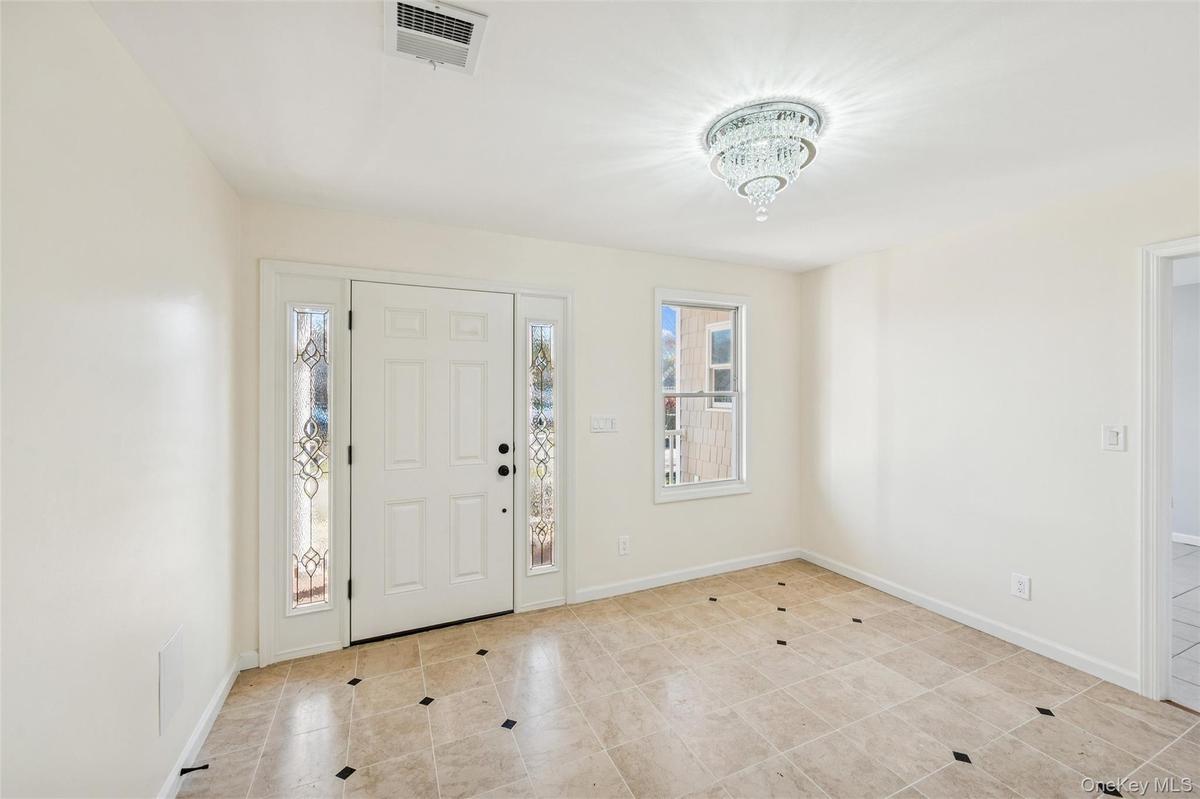 Entryway featuring a white paneled door with decorative sidelights, a tiered crystal chandelier, light-toned tiled flooring with dark accent tiles
