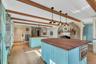Kitchen with blue cabinetry, wooden counters, a stone fireplace, hanging light fixtures, and beam ceiling