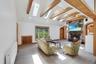 Spacious living room featuring a stone fireplace, a vaulted ceiling with exposed wood beams, multiple skylights, and light-toned wood-finish flooring.