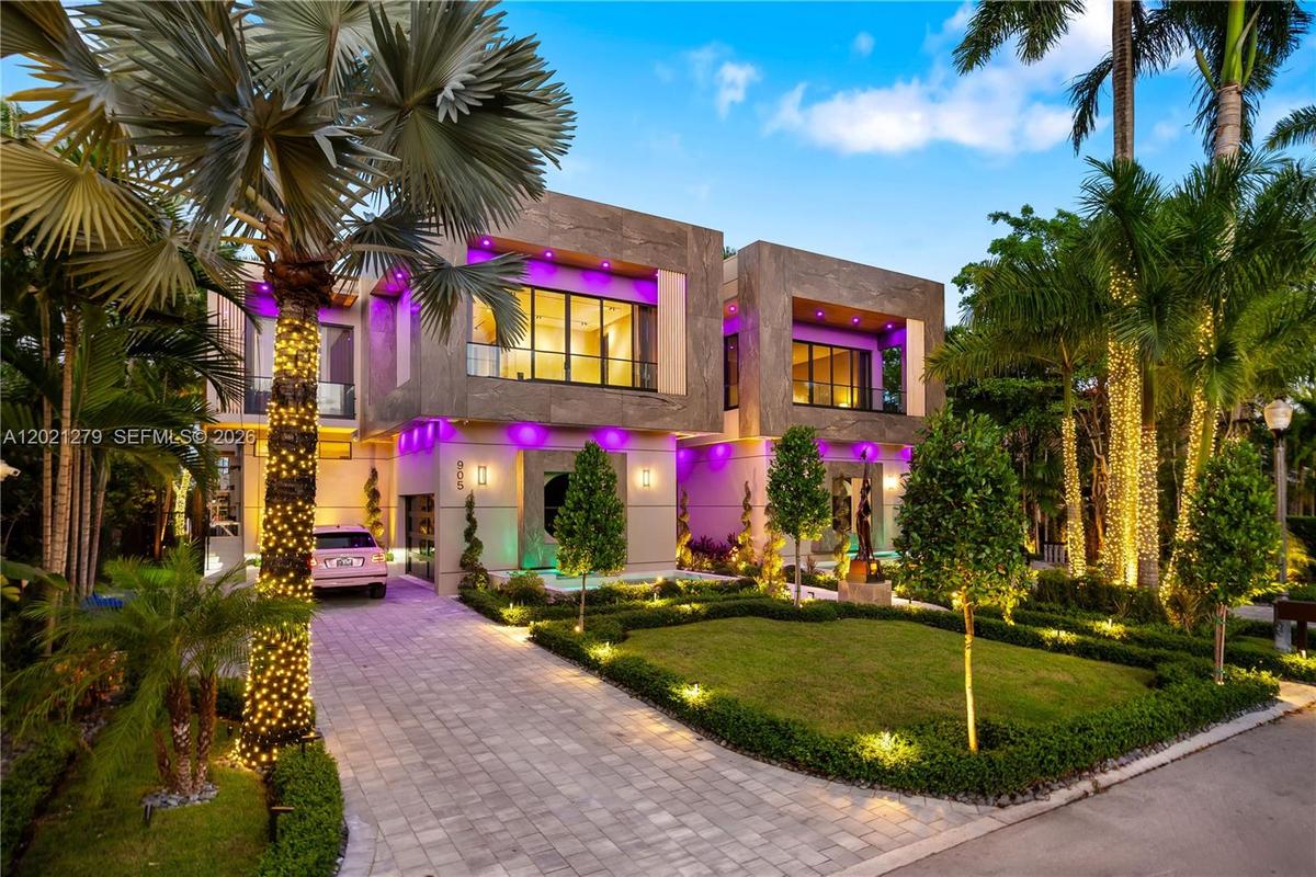 Modern two-story luxury home with stone façade, paver driveway, covered porte-cochère, manicured tropical landscaping, royal palms, and programmable L